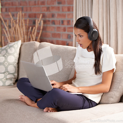 Image of Shocked, home and woman with headphones, laptop and internet connection on sofa listening to music. Female person relax on couch to listen to wow, surprise or fake news announcement online with tech