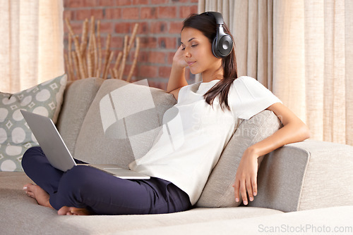 Image of Laptop, headphones and woman on a home sofa listening to music or streaming movies online. Calm female person relax on couch to listen to radio or video with internet connection and technology