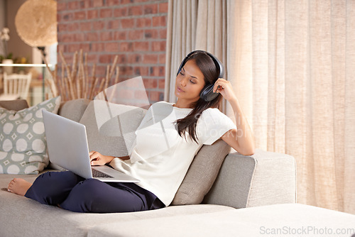 Image of Headphones, laptop and home with woman listening to music, streaming movies and tech. Female person relax on sofa at computer for online radio, elearning blog and remote work with internet connection