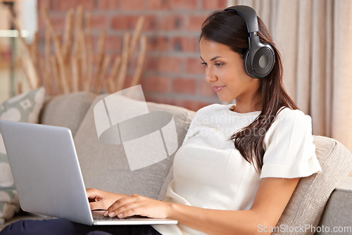 Image of Headphones, home and a woman typing on laptop on home sofa listening to music or streaming movies. Calm female person relax on couch to listen to radio or learning a language with internet connection
