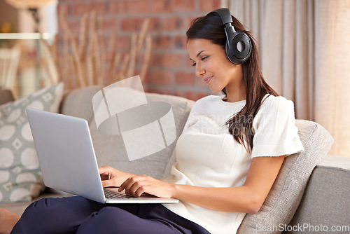 Image of Home, headphones and a woman typing on a laptop and listening to music or audio while streaming online. Happy female person relax on sofa to listen to radio or watch a movie with internet connection