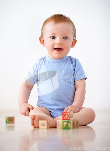 Image of Happy, baby with toy blocks and playing against a white background with smile. Child development or learning, happiness or health wellness and boy toddler play against a studio backdrop on floor