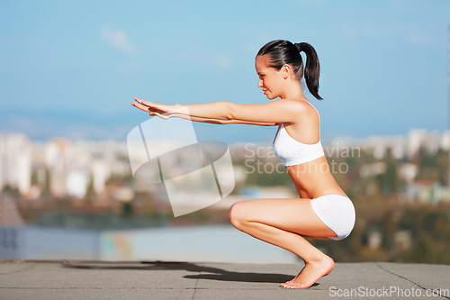 Image of Fitness, woman and body squat on roof top for workout, exercise or training in the city outdoors. Fit and active female squatting, stretching or exercising on floor for balance or healthy wellness