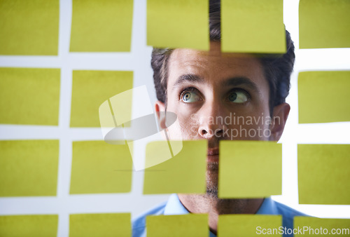 Image of Creative man, face and thinking in sticky note for schedule brainstorming or planning tasks on glass board at office. Male in doubt, decision or problem solving for startup idea strategy at workplace