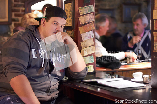 Image of Man portrait, pub and plus size person waiting for a alcohol and beer drink looking serious. Male person, restaurant and alcoholic sitting at a counter at a club with gen z, cool and urban fashion