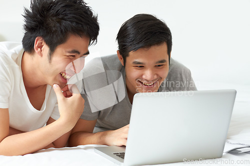 Image of LGBT, laptop and an asian couple in bed together, watching a movie or reading an email in the morning. Love, smile or happy with a gay man and partner streaming an online subscription in the bedroom