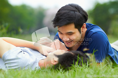 Image of Asian men, gay couple and lying in park, grass or garden with love, care and bonding with kiss in summer. Happy Japanese guy, romantic and relax together on lawn for lgbtq, smile, outdoor in nature