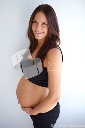Image of Woman, pregnancy portrait and stomach by wall with smile, excited or pride for new life, future or family. Young mom, pregnant and holding belly with happiness, love or care in house with expectation