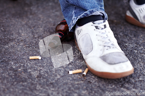 Image of Feet, cigarettes and beer in a road in the city for a man with sneakers smoking and drinking. Shoes, addiction and closeup of tobacco and an alcohol bottle in the outdoor street of an urban town.