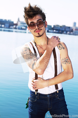 Image of Sunglasses, portrait and serious man by sea with stylish tattoo, body art and fashion. Punk, ocean and trendy male person standing outdoor in Spain with cool clothes, attitude and aesthetic mockup.