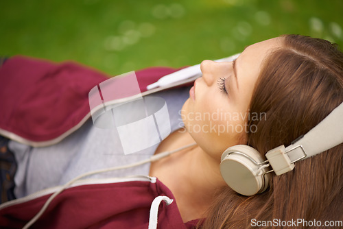 Image of Woman, student and headphones for music on grass to relax, summer and audio streaming subscription. Girl, campus lawn and park with meditation sound, sleep and peace for listening, radio and podcast