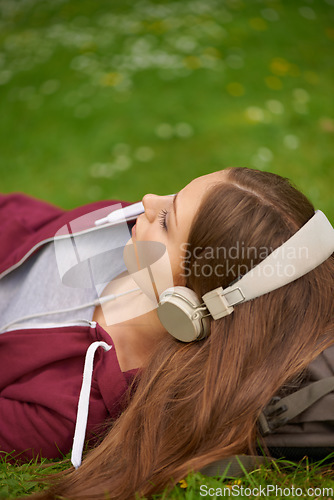 Image of Woman, student and headphones for music on lawn to relax, summer and audio streaming subscription. Girl, campus grass and park with meditation sound, sleep and peace for listening, radio and podcast