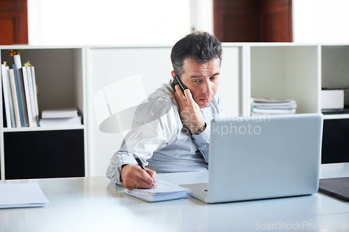 Image of Consultant, businessman with smartphone on a call and with laptop writing notes in a notebook at his office. Customer service or online communication, networking and male person a cellphone at desk