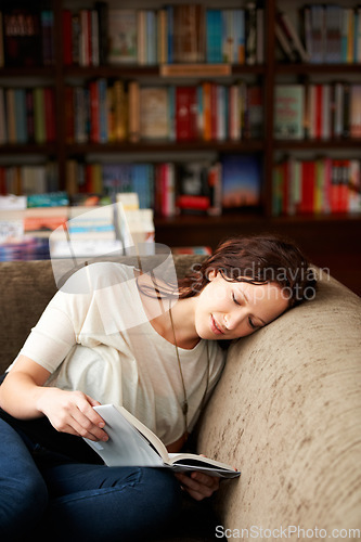 Image of Calm, library and woman reading a book on a sofa for literature while relaxing with shelves. Rest, happy and female person with a smile enjoying a fantasy story or novel on couch in bookstore or shop