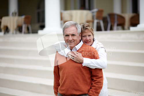 Image of Hug, portrait and an old couple on hotel steps for travel, vacation or tourism in luxury accommodation. Love, retirement or hospitality with a senior man and woman hugging on a resort staircase