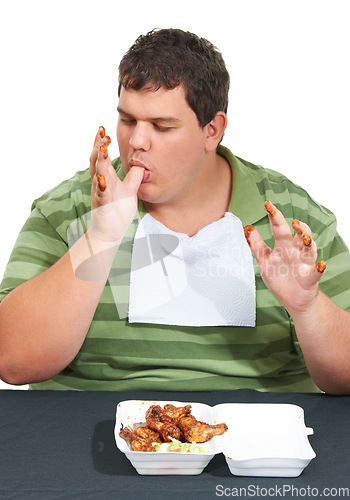 Image of Plus sized, eating and man with junk food, unhealthy diet and hungry person isolated on white background. Chicken, weight loss and food addiction problem, male model licking finger at table in studio