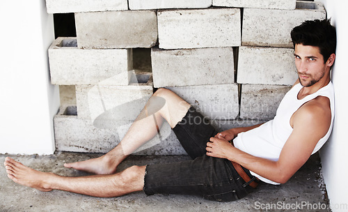 Image of Portrait of sexy man, handsome and wall background with beauty, glow and confidence sitting on floor. Attractive, confident and serious face of male model on brick backdrop with thoughtful expression