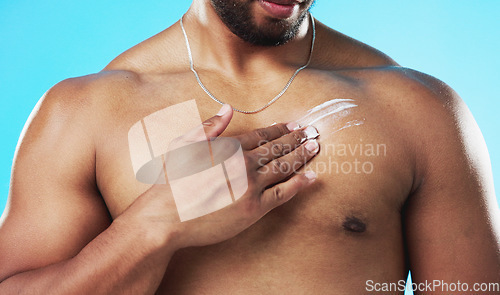 Image of Skincare, applying and man with cream on his chest isolated on a blue background in a studio. Moisturizing, sexy and male model with sunscreen, lotion or moisturizer on his body for grooming