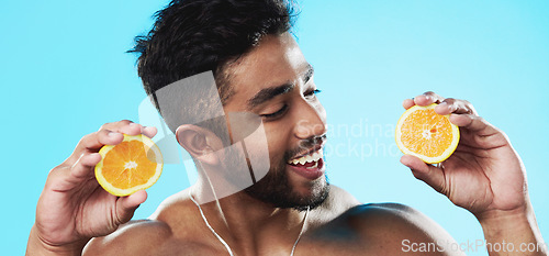 Image of Orange, skincare and face of man in studio for beauty, wellness and citrus treatment on blue background. Fruit, facial and portrait of indian male model excited for organic vitamin c skin cosmetics
