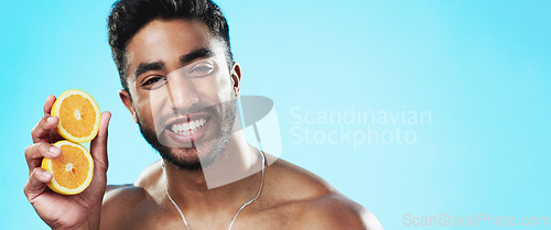 Image of Beauty, orange and face of man in studio for skincare, wellness and citrus treatment on blue background. Fruit, facial and portrait of indian male model excited for organic vitamin c skin cosmetics