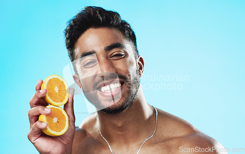 Image of Happy, orange and face of man in studio for skincare, wellness and citrus treatment on blue background. Fruit, facial and portrait of indian male model excited for organic vitamin c skin cosmetics