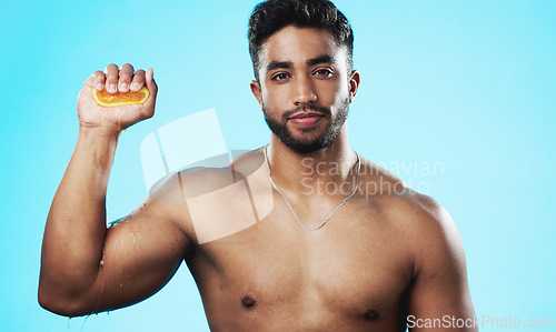 Image of Skincare, squeeze and face of man with orange in studio for beauty, wellness and citrus treatment on blue background. Fruit, facial and portrait of indian guy model with organic, anti aging vitamin c
