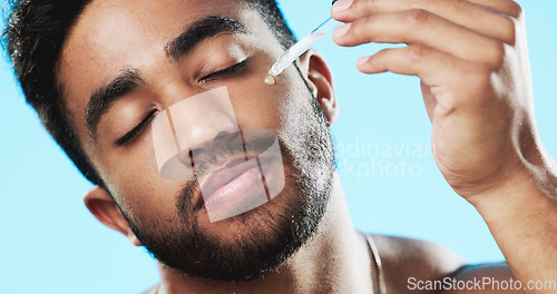 Image of Skincare, health and man with face serum in a studio with a beauty, grooming and face routine. Wellness, cosmetic and male model with a facial oil pipette for a skin treatment by a blue background.