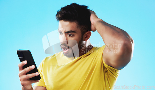 Image of Phone, wow or bad news with a man reading a negative text message in studio on a blue background. Mobile, contact and surprise with a young male looking shocked by a social media post or announcement