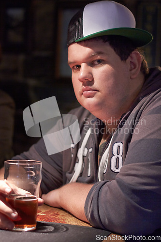 Image of Man portrait, pub beer and plus size person waiting for a alcohol and drink looking serious. Male person, restaurant and glass pint sitting at a counter at a club with gen z, cool and urban fashion