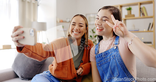 Image of Phone, selfie and friends on a living room sofa taking a profile picture together for social media. Digital, women and girl friend in a home with peace sign posing on a mobile for web app in house