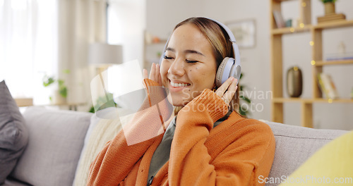 Image of Headphones, sofa and happy woman listening to music for mental health, youth radio and streaming at home. Young asian person or relax with audio technology in living room, couch or apartment for Kpop