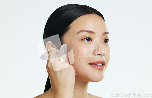 Image of Gua sha, beauty and woman massaging face isolated on a white background in a studio. Spa, skincare and an Asian girl with a product to massage for facial relaxation, treatment and anti aging