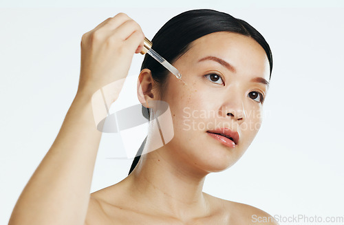 Image of Asian woman, face and oil serum for beauty, facial skincare or dropper of hyaluronic acid in studio. Female model, cosmetics product and liquid collagen of glow, shine or thinking on white background