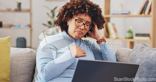 Image of Laptop, bad news and loss with a woman on a sofa in the living room of her home feeling unhappy or emotional. Computer, shock and grief with a sad young female reading an email or social media feed