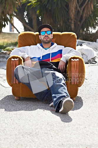 Image of Portrait, man with sunglasses and street or urban, fashion and relax with cool streetwear style in the city. Person, face and stylish model with cap relaxing, chair or outdoor couch and sofa