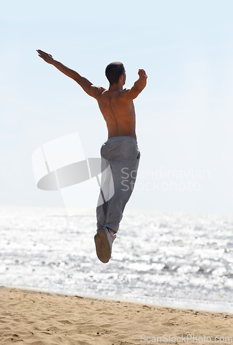 Image of Freedom, beach and man jump at the ocean with energy celebration and positivity on sky background. Rear view, jumping and and male person excited for milestone, success and achievement in nature