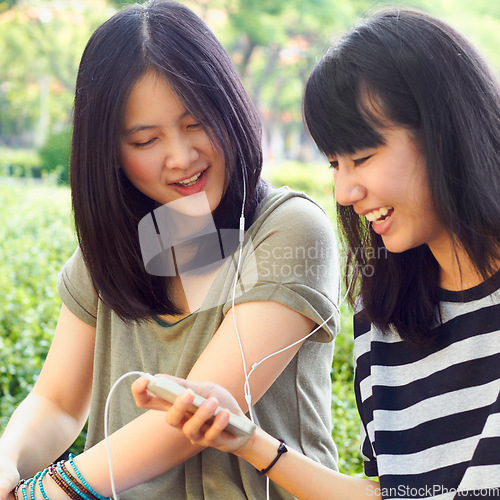 Image of Asian women, students together and earphones with comic laugh, funny music video and meme at campus. Japanese girl, friends and audio streaming with smartphone, sharing and listen with smile in park