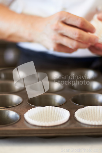 Image of Cupcake tray, person hands and baking in kitchen with muffin wrapper and cooking closeup in bakery. Prepare, paper cup and food with chef in restaurant, coffee shop or cafe with sweet cake or pastry