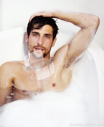 Image of Portrait, hygiene and a sexy man in a bath in his home for soap cleaning, grooming or body care. Health, nude and beauty with a handsome young man lying in a luxury bathroom to relax or refresh