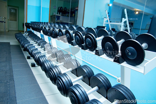 Image of Dumbbells, empty gym interior and fitness with equipment for wellness, healthy bodybuilding or training. Exercise, workout or health club with metal weights on shelf, strong body development or sport