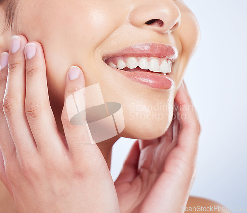 Image of Skincare, smile and hands on face of woman in studio for healthy skin, glow or treatment on blue background. Happy, beauty and mouth of lady model with luxury hydration cosmetics, lip gloss or makeup