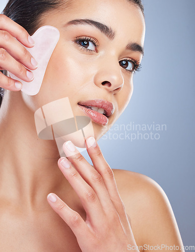 Image of Gua sha, crystal and portrait of asian woman with skincare tool in studio for anti aging or fine lines on grey background. Rose quartz, stone and lady face wellness model with facial beauty massage