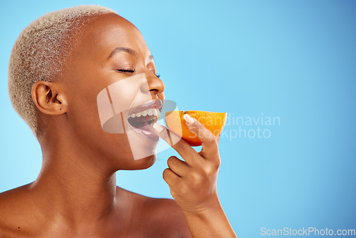 Image of Orange, skincare and nutrition with a model black woman in studio on a blue background biting fruit. Food, beauty and natural with a happy young female person eating a snack for health or wellness