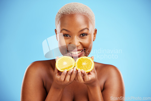 Image of Portrait, skincare and fruit or nutrition with a black woman in studio on a blue background for health. Smile, beauty and orange with a happy young female person holding food for natural wellness