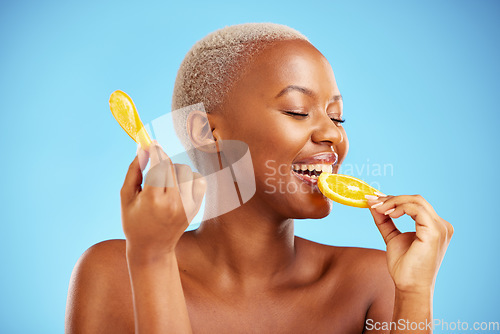 Image of Orange, beauty and nutrition with a model black woman in studio on a blue background biting fruit. Food, skincare and natural with a happy young female person eating a snack for health or wellness