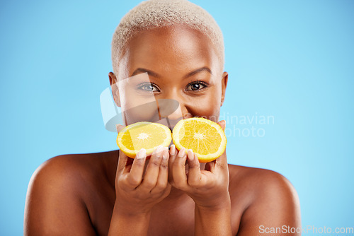 Image of Portrait, beauty and fruit with a model black woman in studio on a blue background for natural wellness. Face, skincare and orange with a happy young female person holding a fresh snack for health