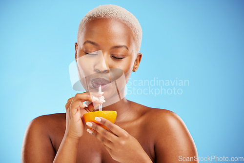 Image of Black woman, vitamin C and drinking orange for diet or natural nutrition against a blue studio background. Calm African female person with citrus fruit, drink and straw for healthy wellness or juice