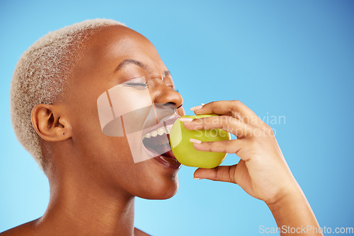 Image of Black woman, apple and bite in diet, nutrition or health and wellness against a blue studio background. Face of African female person eating natural organic fruit for vitamin, fiber or food on mockup