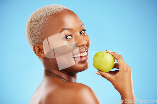 Image of Happy black woman, portrait and apple for diet, nutrition or health and wellness against a blue studio background. Face of African female person with natural organic fruit for vitamin, fiber or food