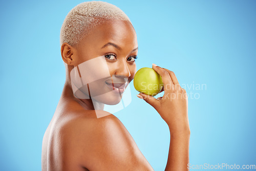 Image of Happy black woman, portrait and apple for nutrition or healthy diet against a blue studio background. African female person smile with natural organic green fruit for food snack, health and wellness